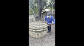A chicken farmer is putting the finishing touches to a handmade bamboo chicken cage that he made.