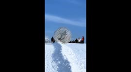 Tourists take a dizzying ride down snowy slope in an inflatable ball