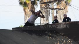 Armed police confront a shirtless man on top of a building in LA